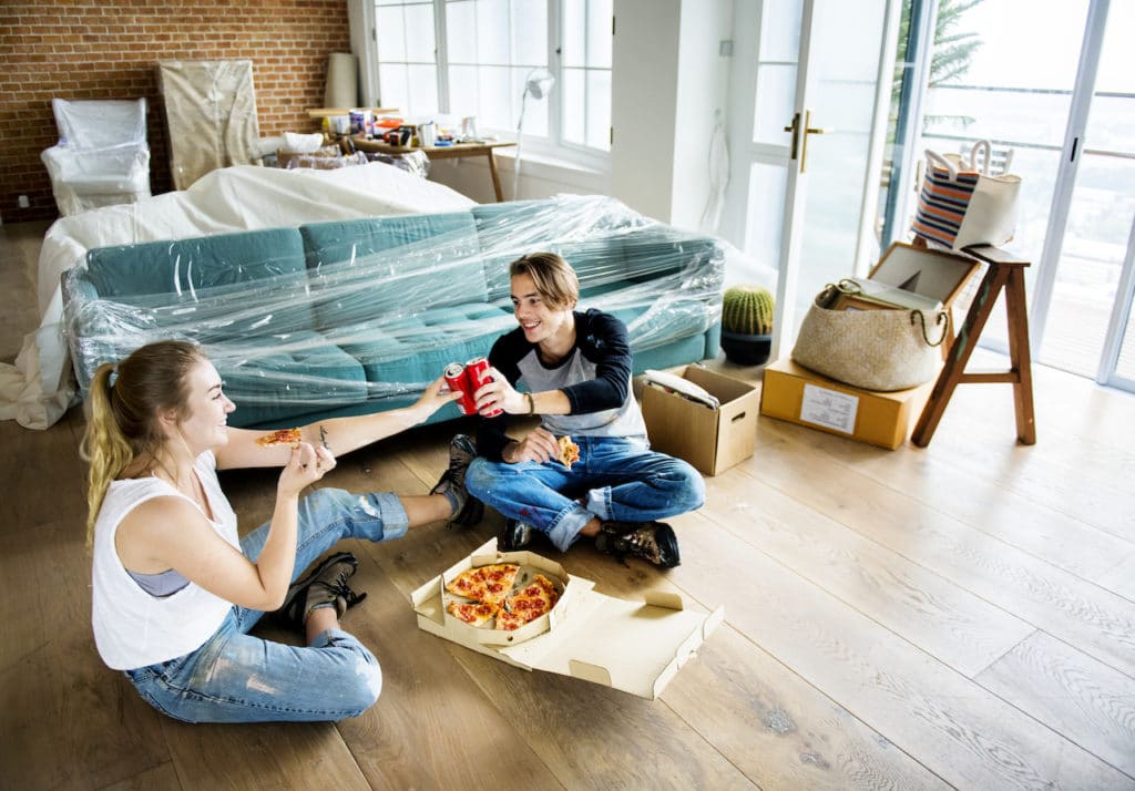 two people sitting on floor of new apartment eating pizza