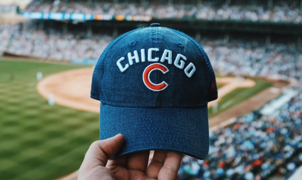 blue cubs hat being held up with wrigley field in the background