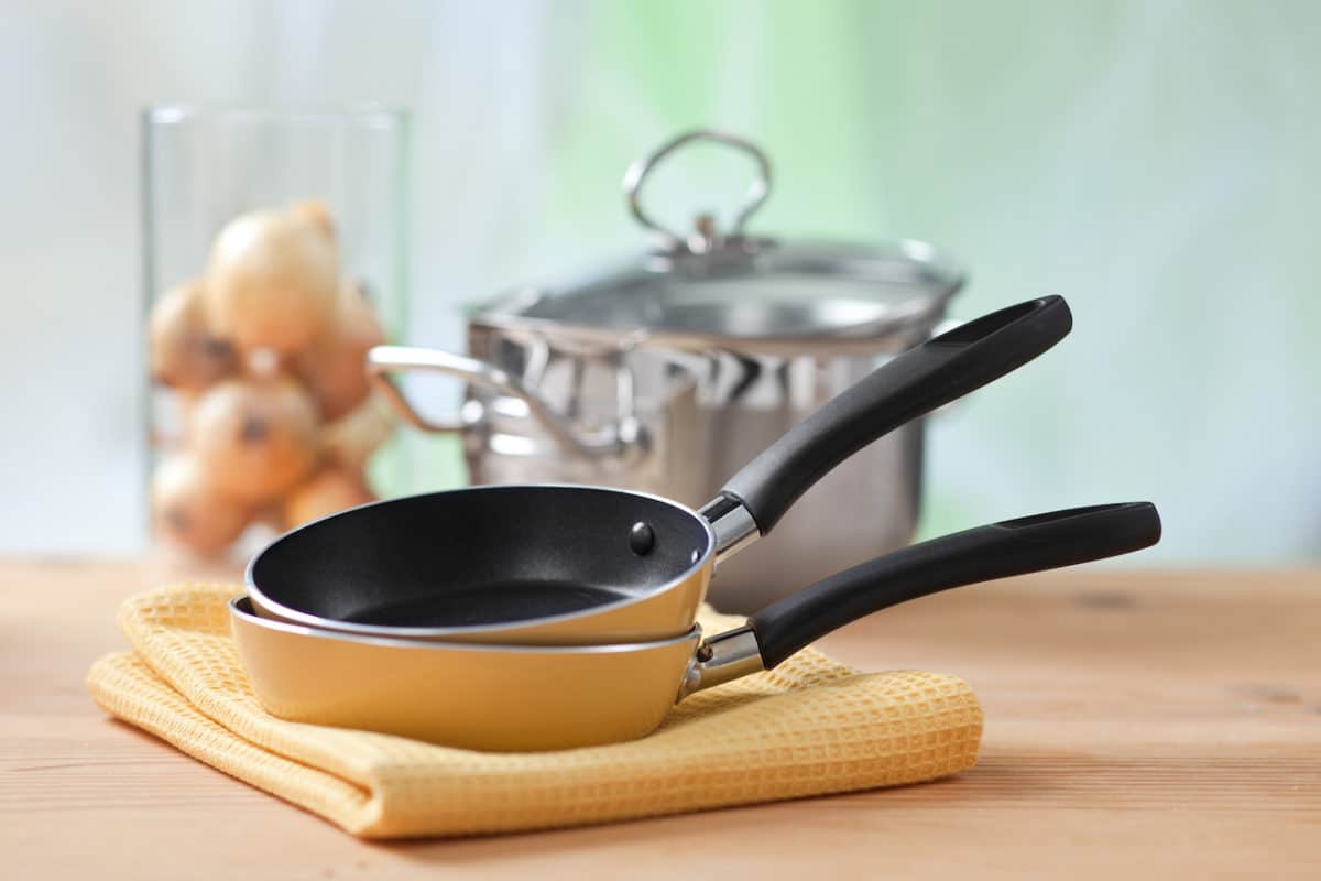 yellow towel with clean cooking pans on top of it and a silver pot in the background
