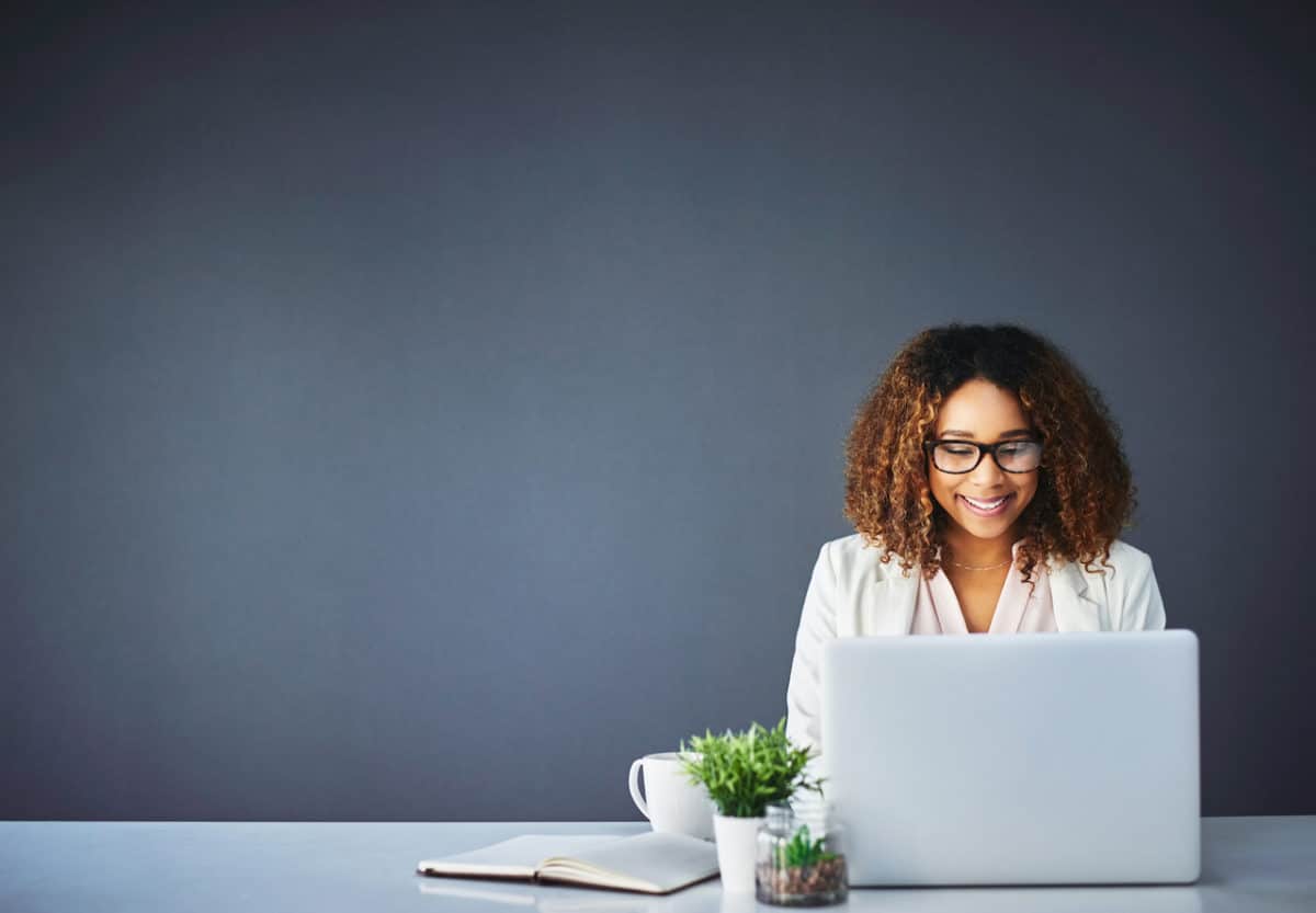 woman at desk typing on laptop and smiling
