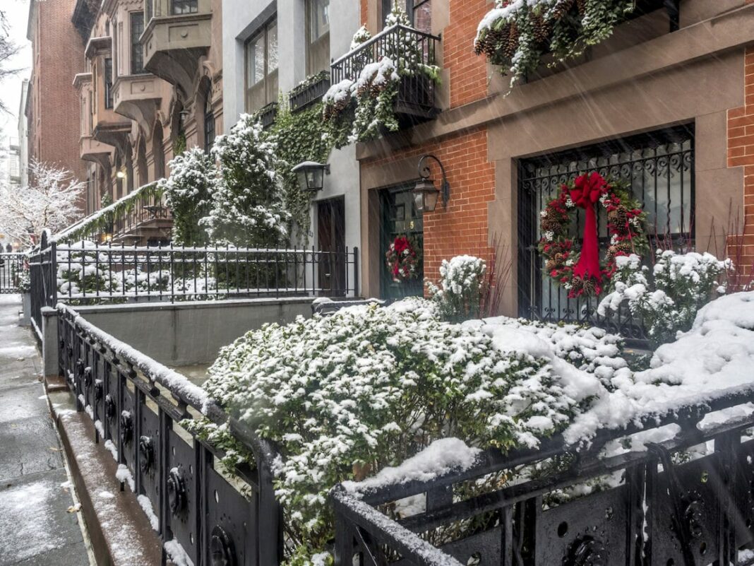 Brick houses with snow covered plants in front and a christmas wreath on a door