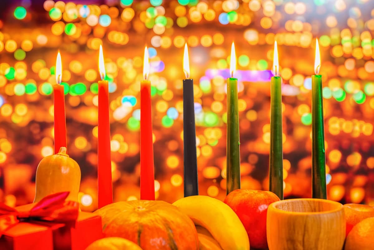 Kwanzaa celebration concept with seven candles red, black and green, gift box, pumpkin, bowl and fruit on light blur bokeh background, close up