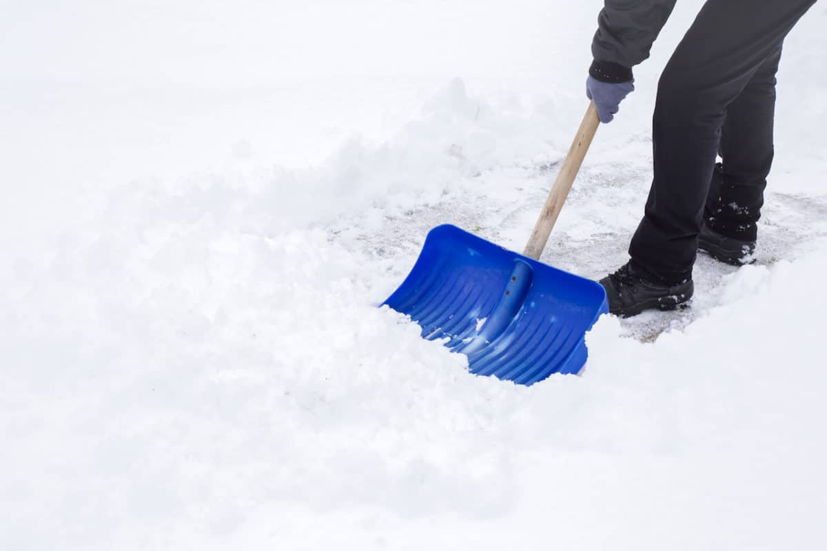 Man cleaning snow off sidewalk with shovel on winter day