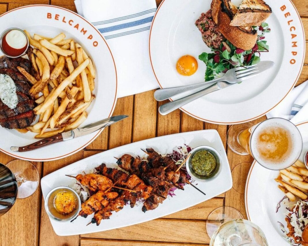 Table filled with Belcampo plates with steak, fries, chicken skewers and salad on it