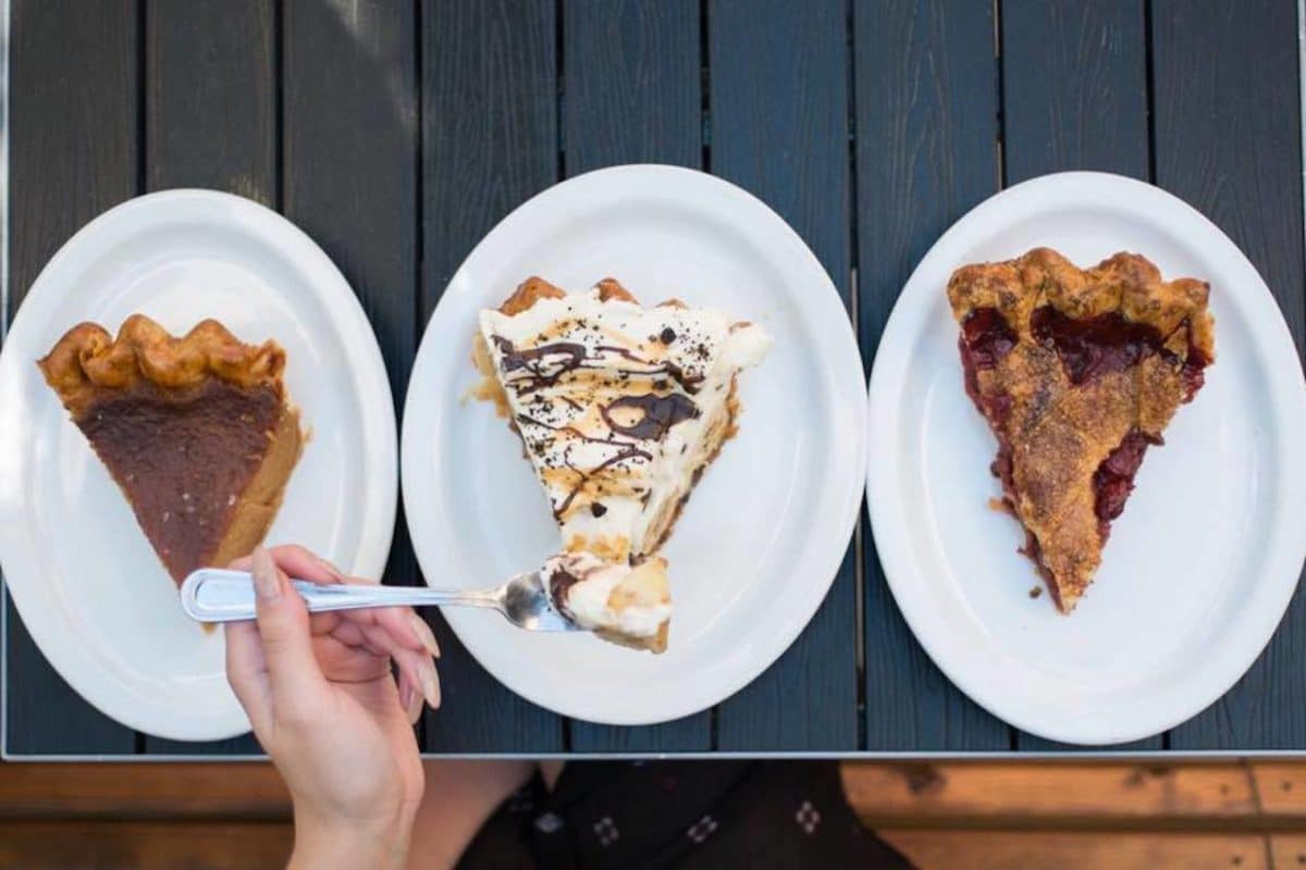 Three plates with different pies on them and woman using form to hold up a bite of one