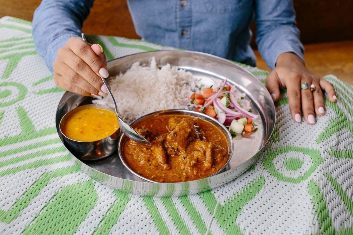 close up of indian food on plate with hands using a fork to eat it