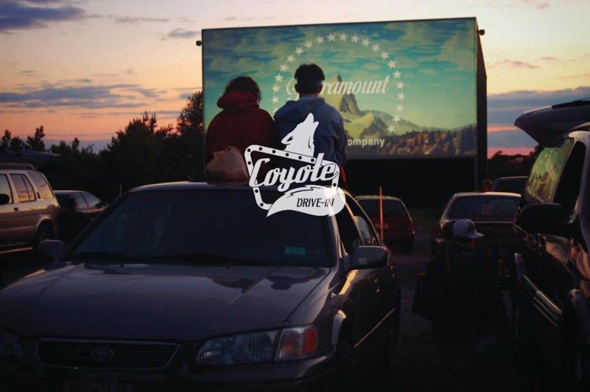 Two people sitting on top of car watching movie at drive in theater