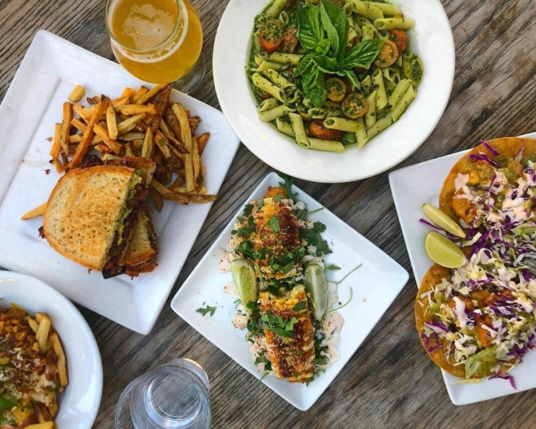 Table with beer, pasta, corn on the cob, and other vegan menu items
