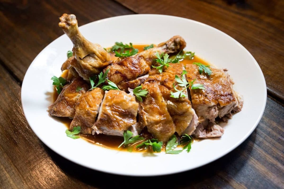Plate with duck leg and strips on it in a sauce with green herbs on top