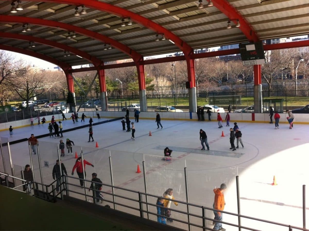 Covered outdoor ice rink with people skating around on a sunny day