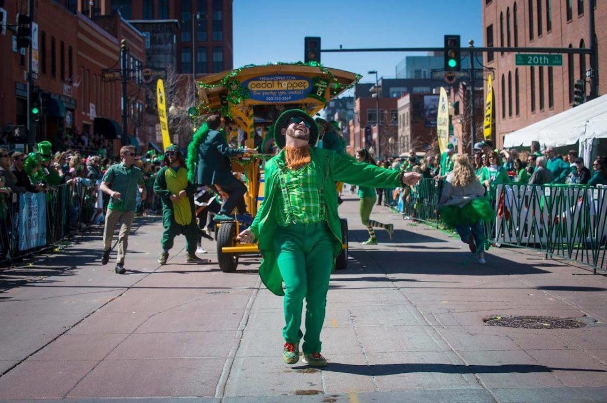 man in leprechaun outfit leading st. patrick's day parade float behind him while crowd watches on