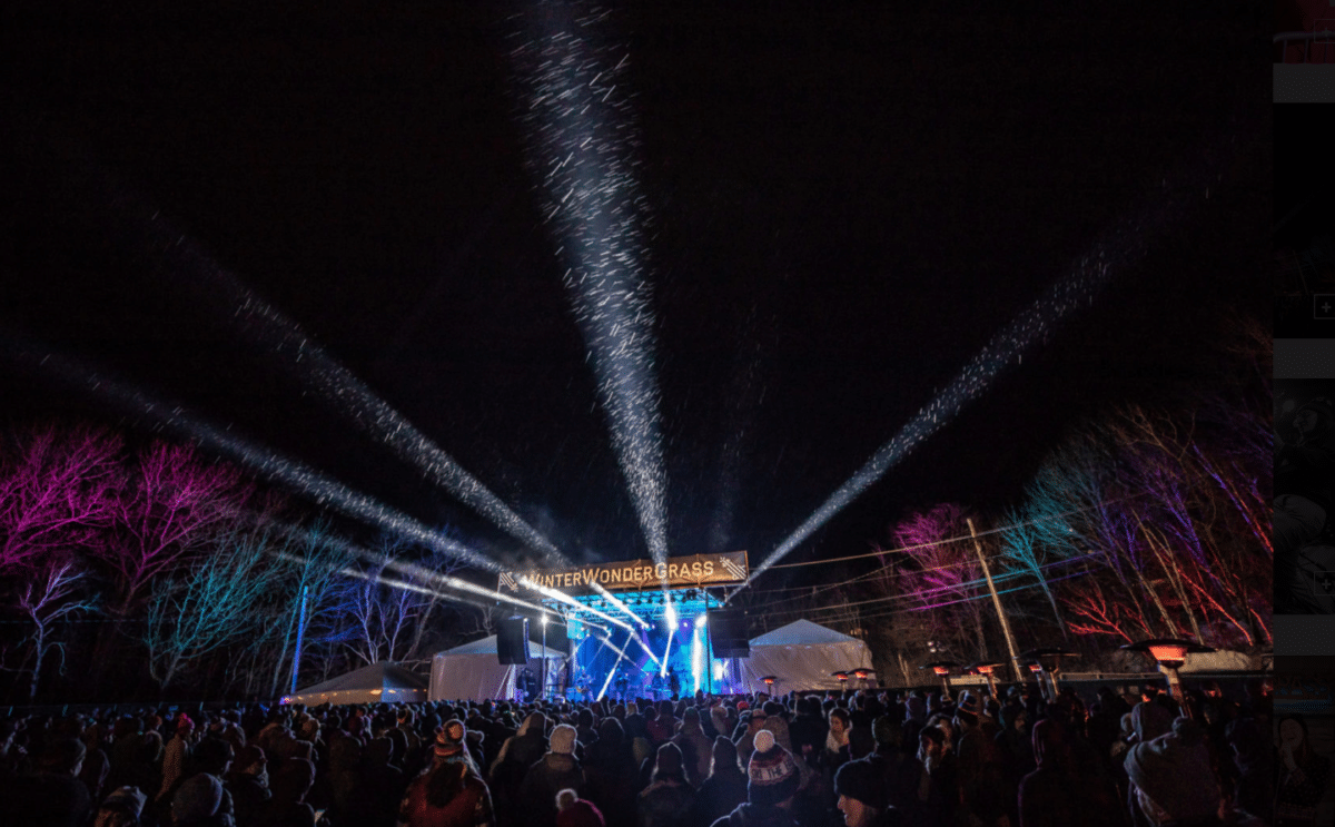nighttime shot of stage and crowd with lights beaming at concert