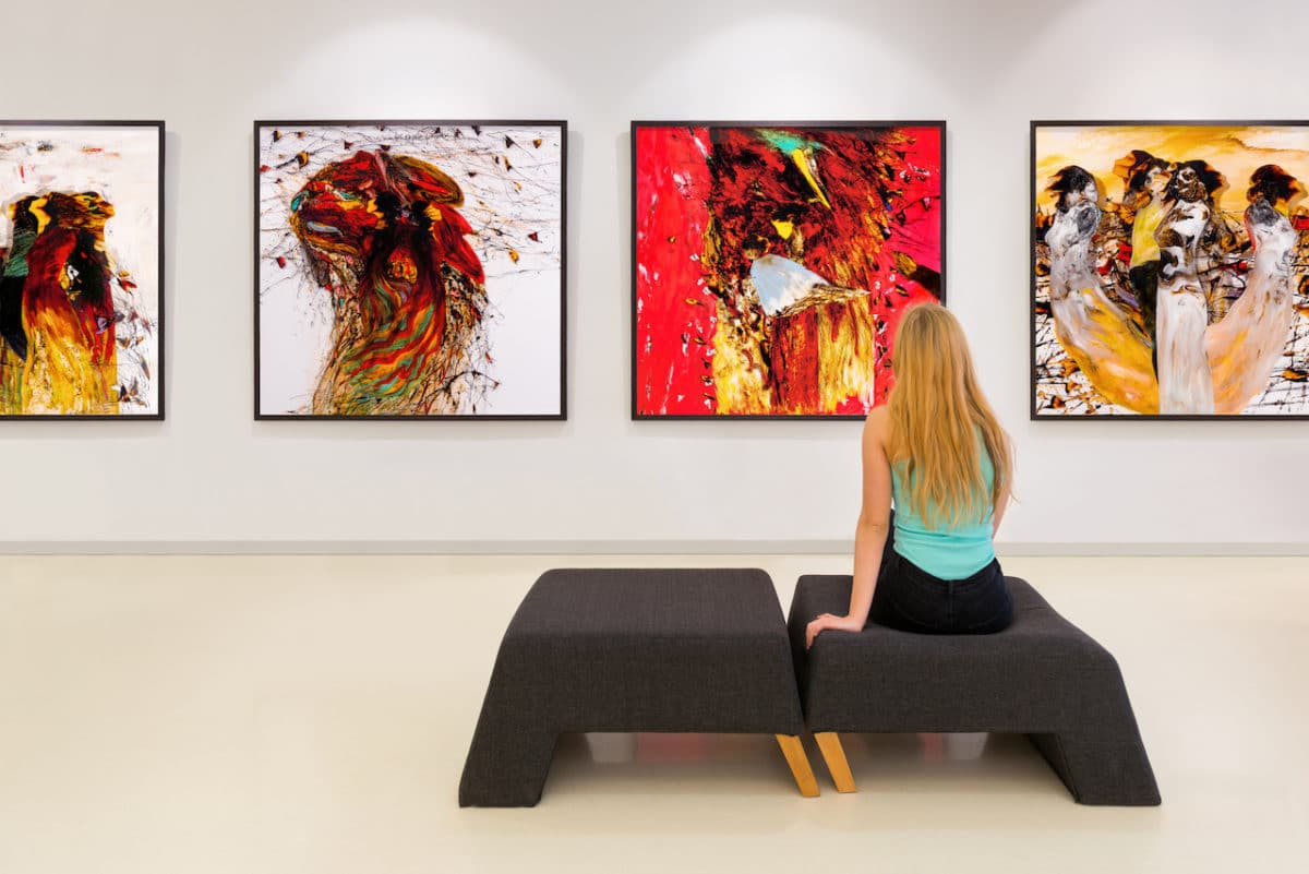 Young woman sitting on bench in art gallery looking at art on wall