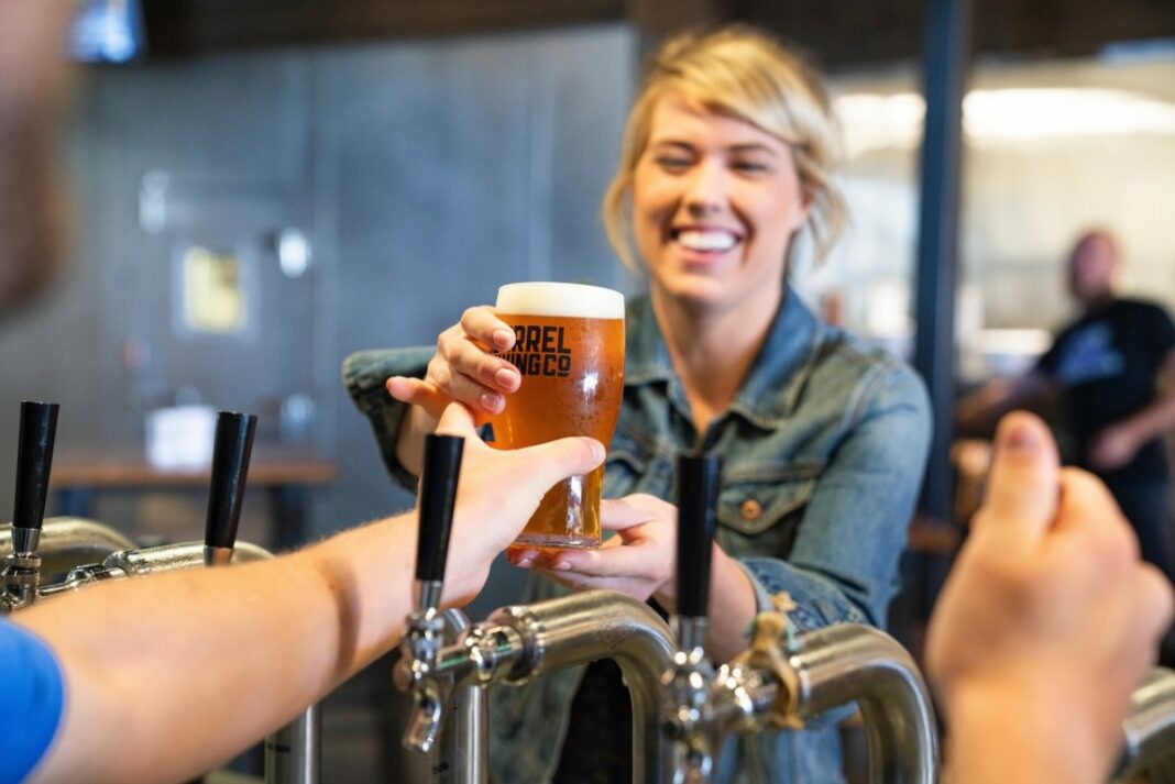 female behind bar handing customer their beer over beer taps