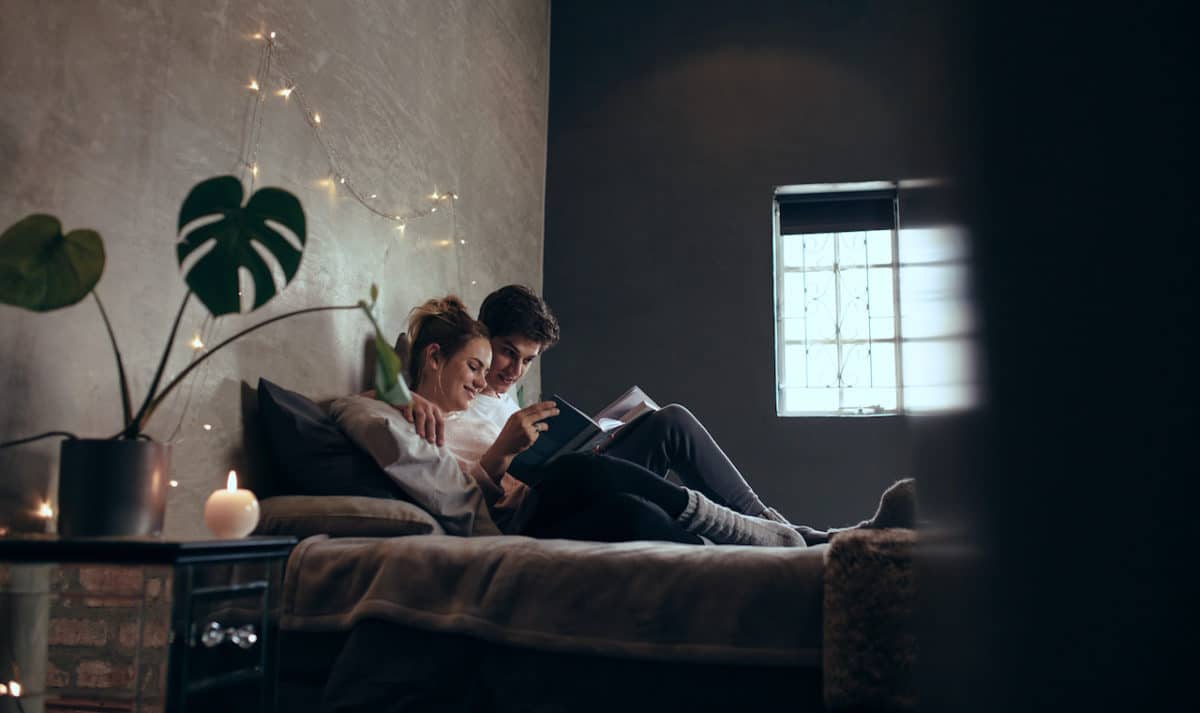 couple smiling and reading book on bed together