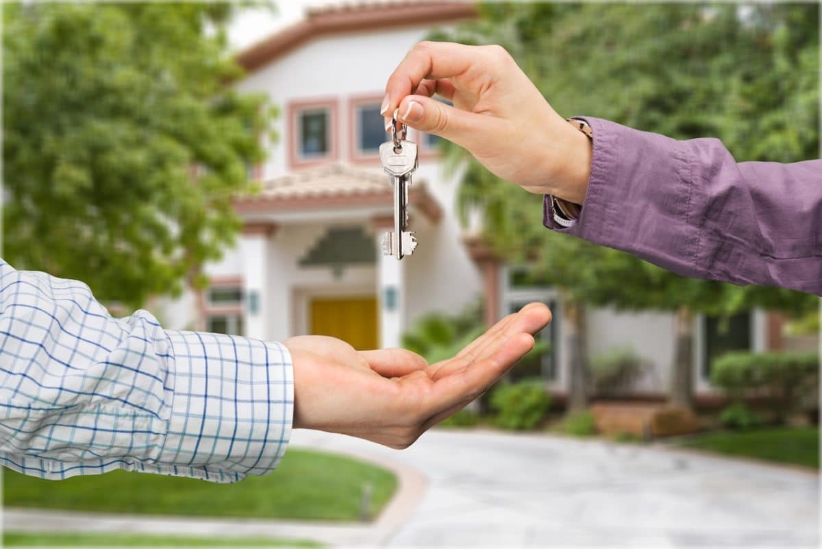 two people exchanging house keys with house in background