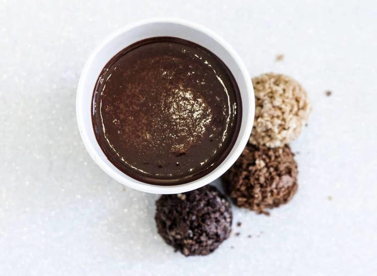 dark hot cocoa in white cup and three cocoa power balls around the cup