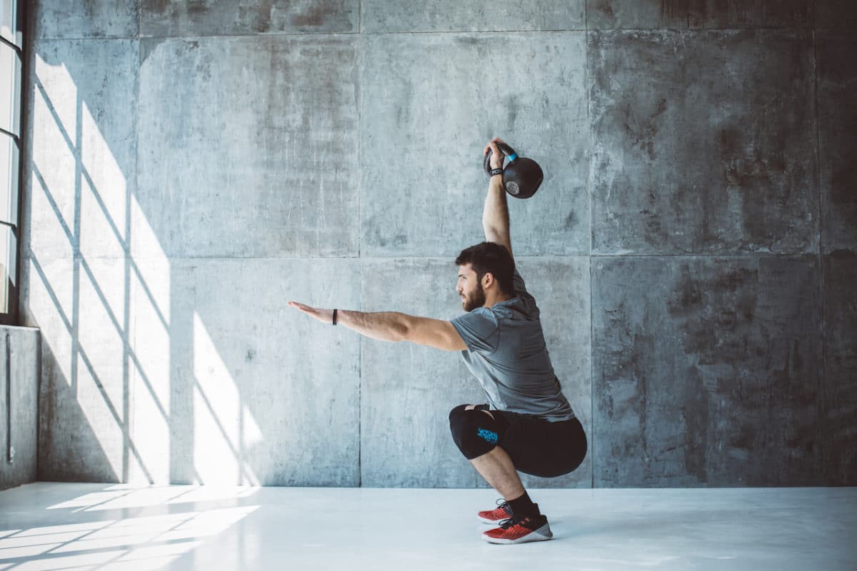 man squatting in empty loft with raised kettlebell
