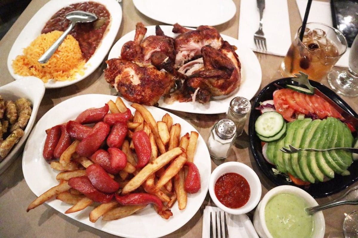 table full of plates of food with chicken, fries, sauces and utensils