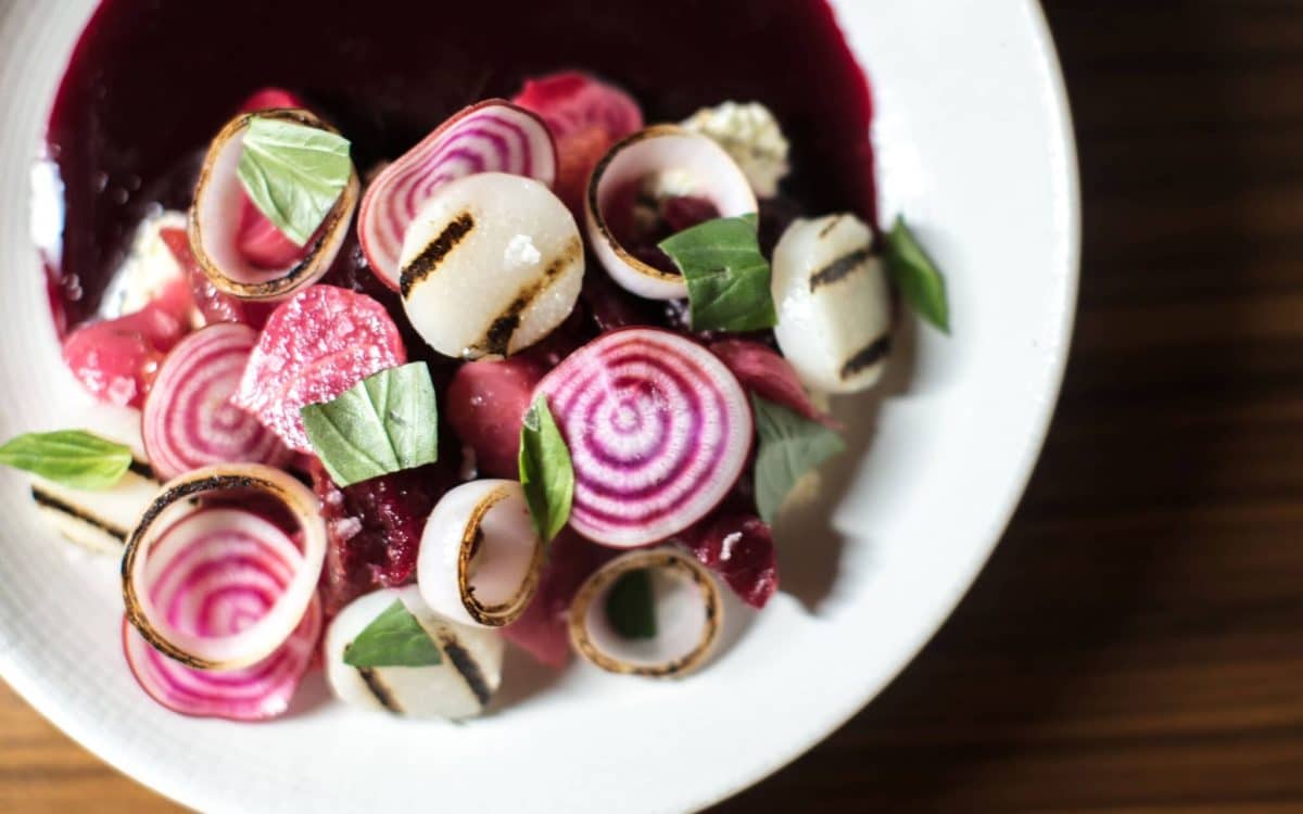 White plate on table with purple, white and green veggies and brown sauce