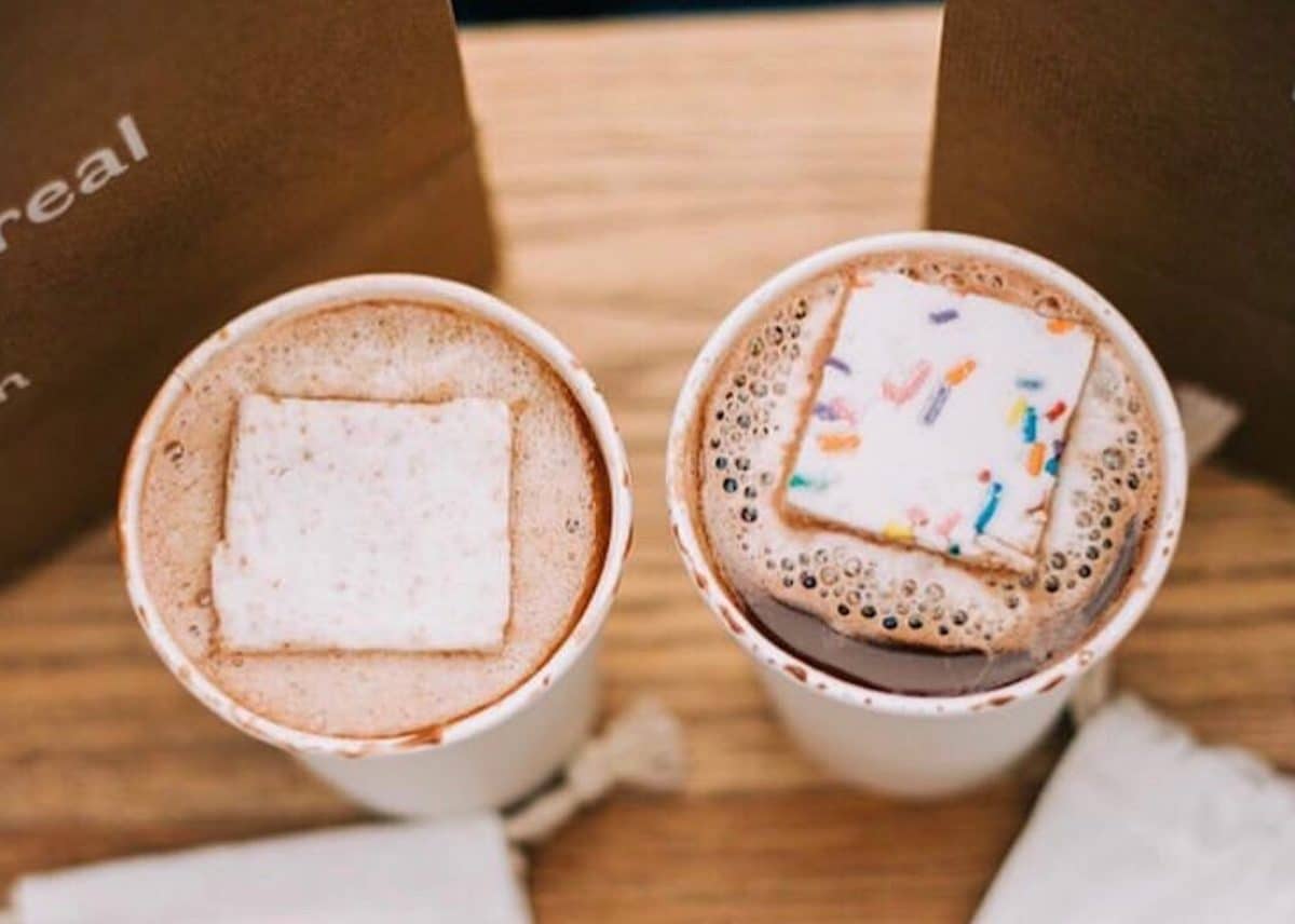 two hot chocolates in paper cups with a giant marshmallow in each