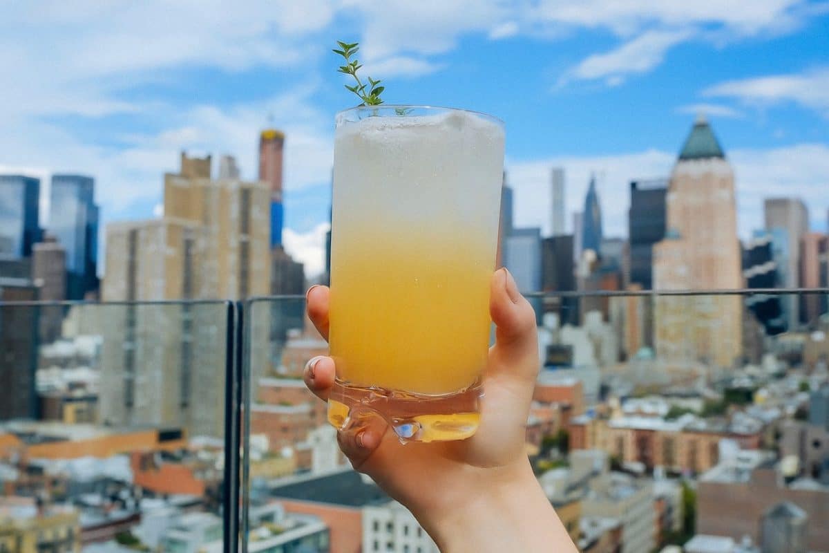 woman holding up cocktail on rooftop bar overlooking manhattan