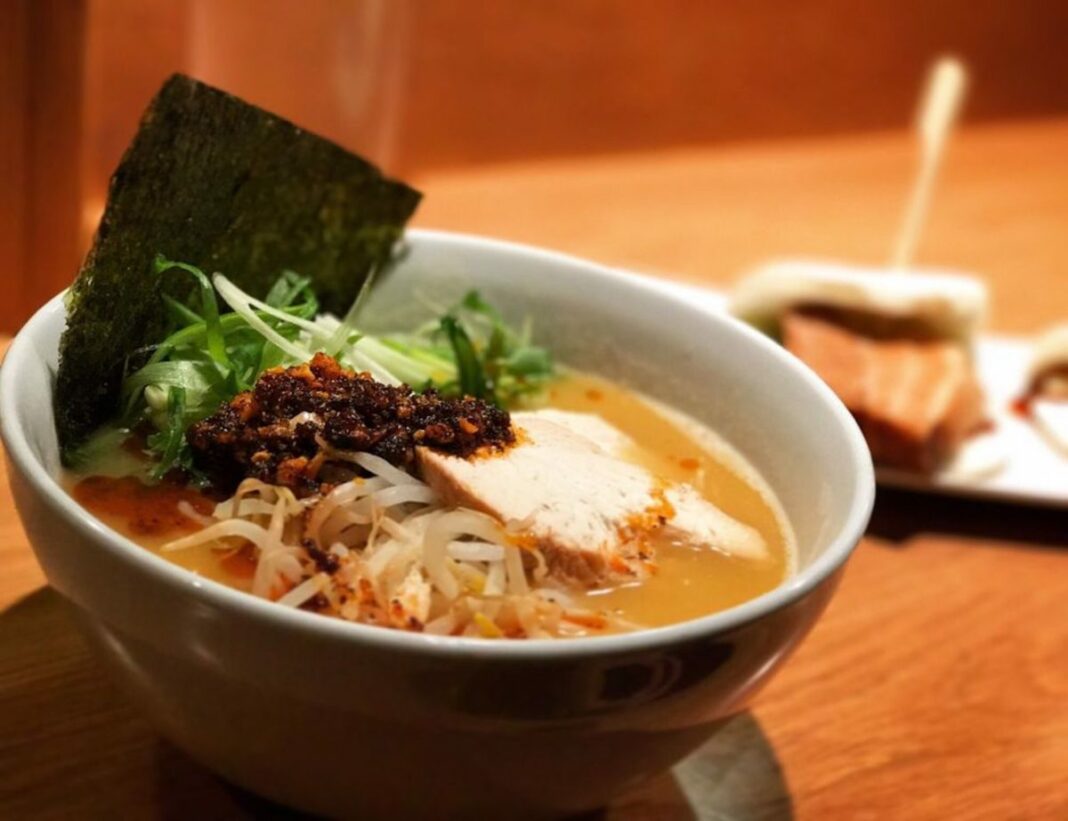 ramen bowl on table full of broth, noodles, meat, and greens