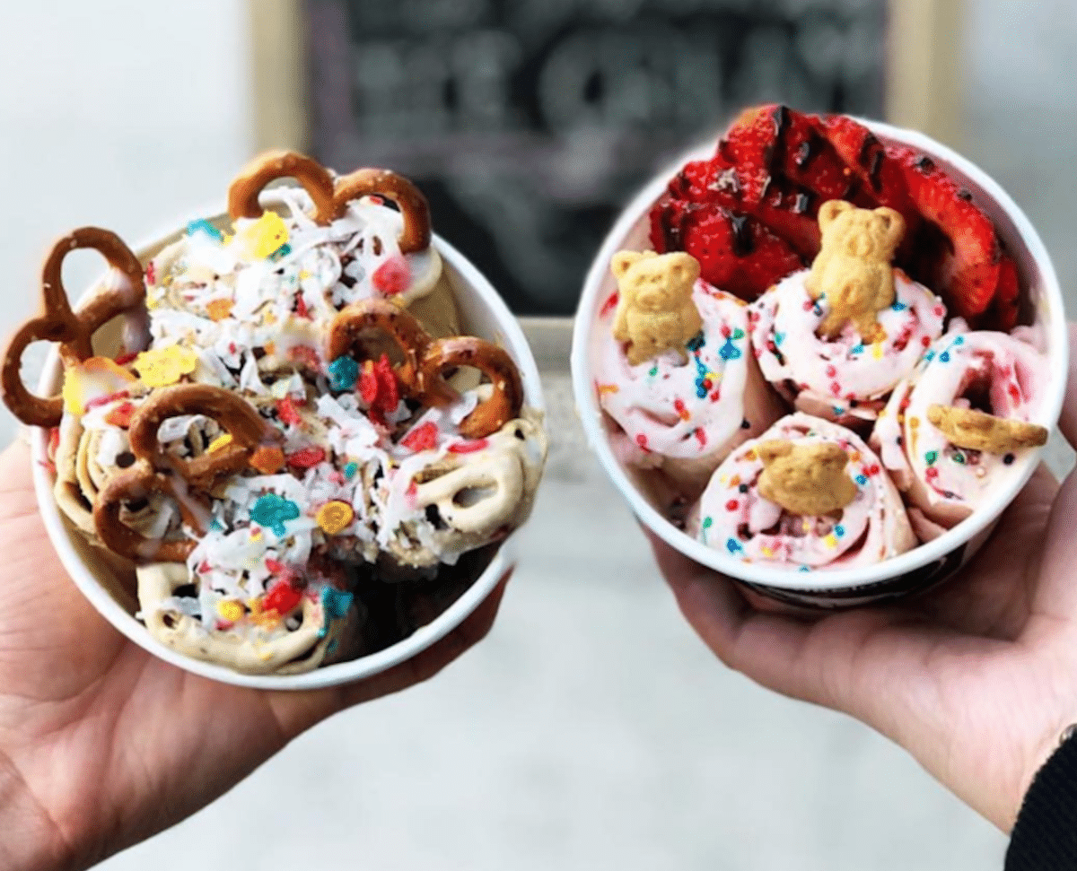 two hands holding up ice cream cups with lot of toppings