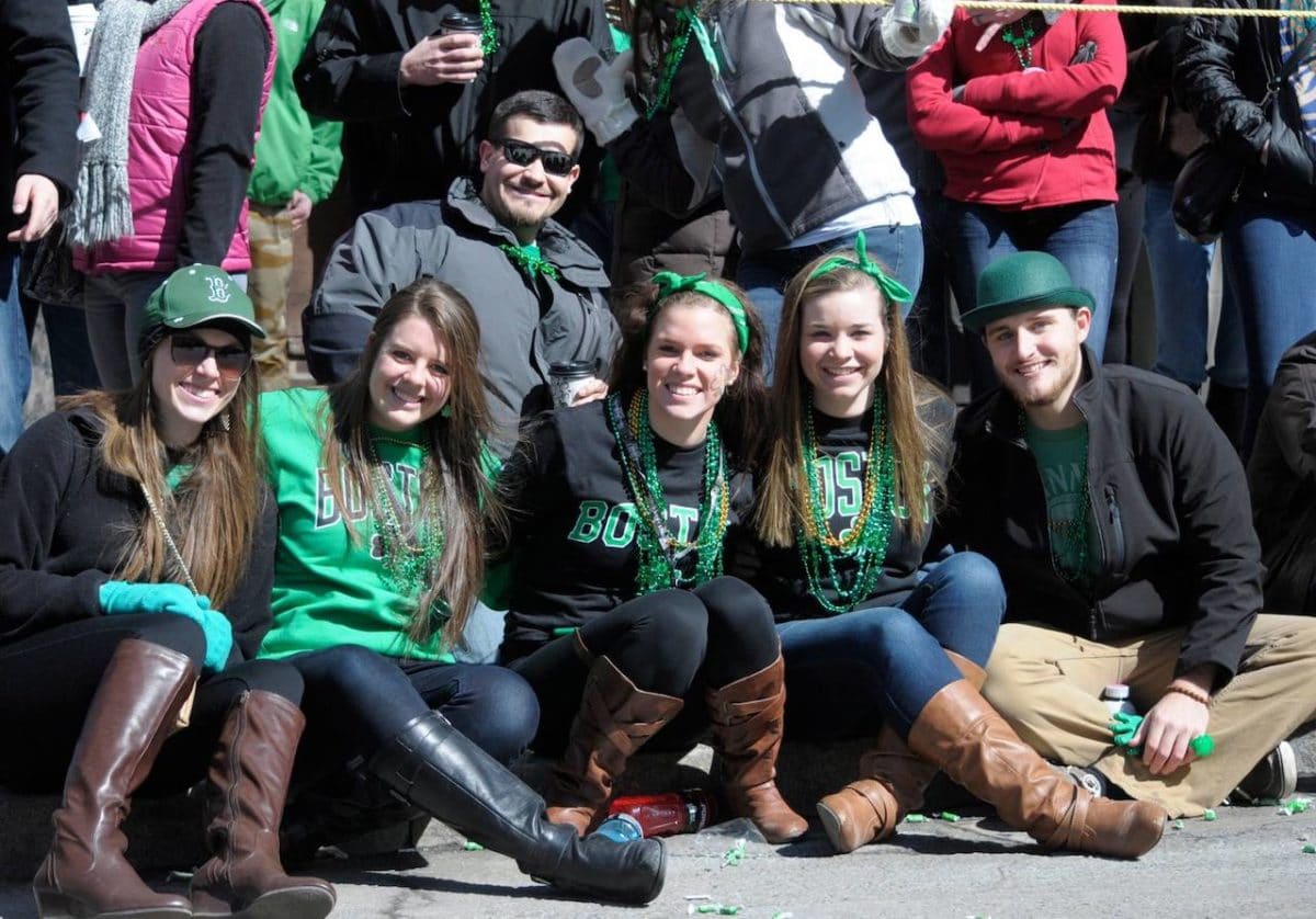 group of friends wearing green sitting on ground watching parade and posing for the camera
