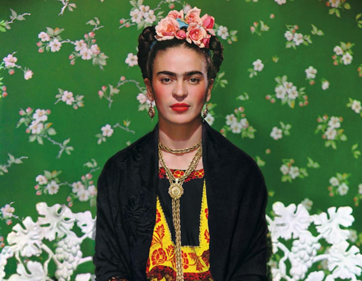 close up of Frida Kahlo sitting in front of a green and white wallpaper
