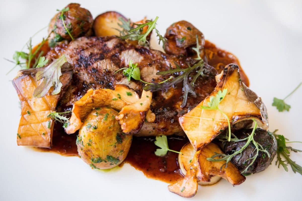 white dish with mushrooms, steak, and green sprouts in a brown sauce