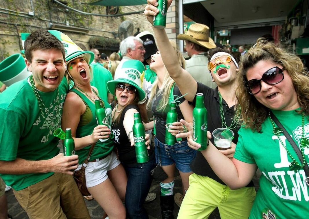group of people wearing green, drinking out of green bottles, and singing at the camera