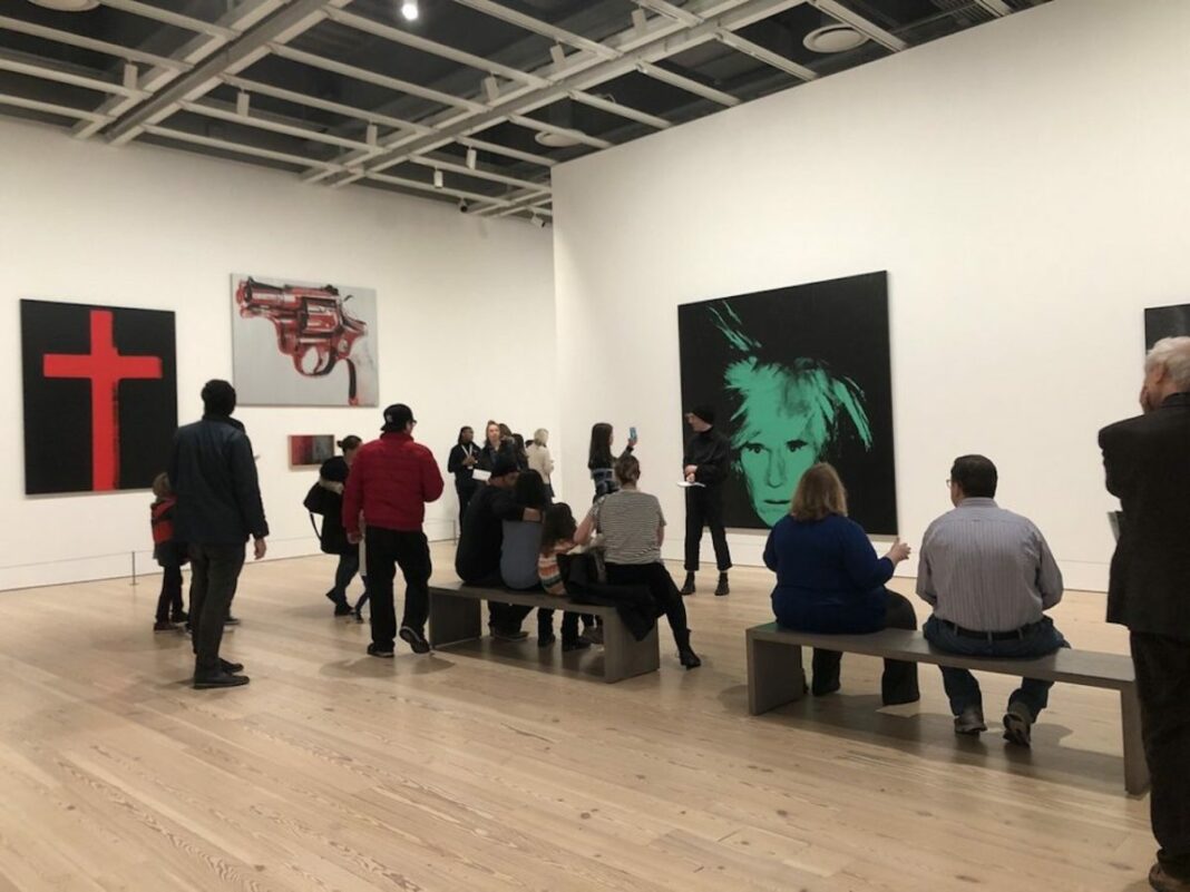 people listening to tour guide tell them about andy warhol exhibit behind her