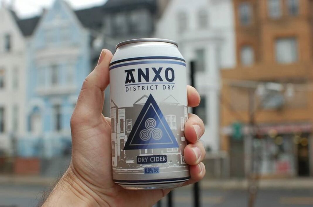 hand holding can of anxo cider up with houses in background