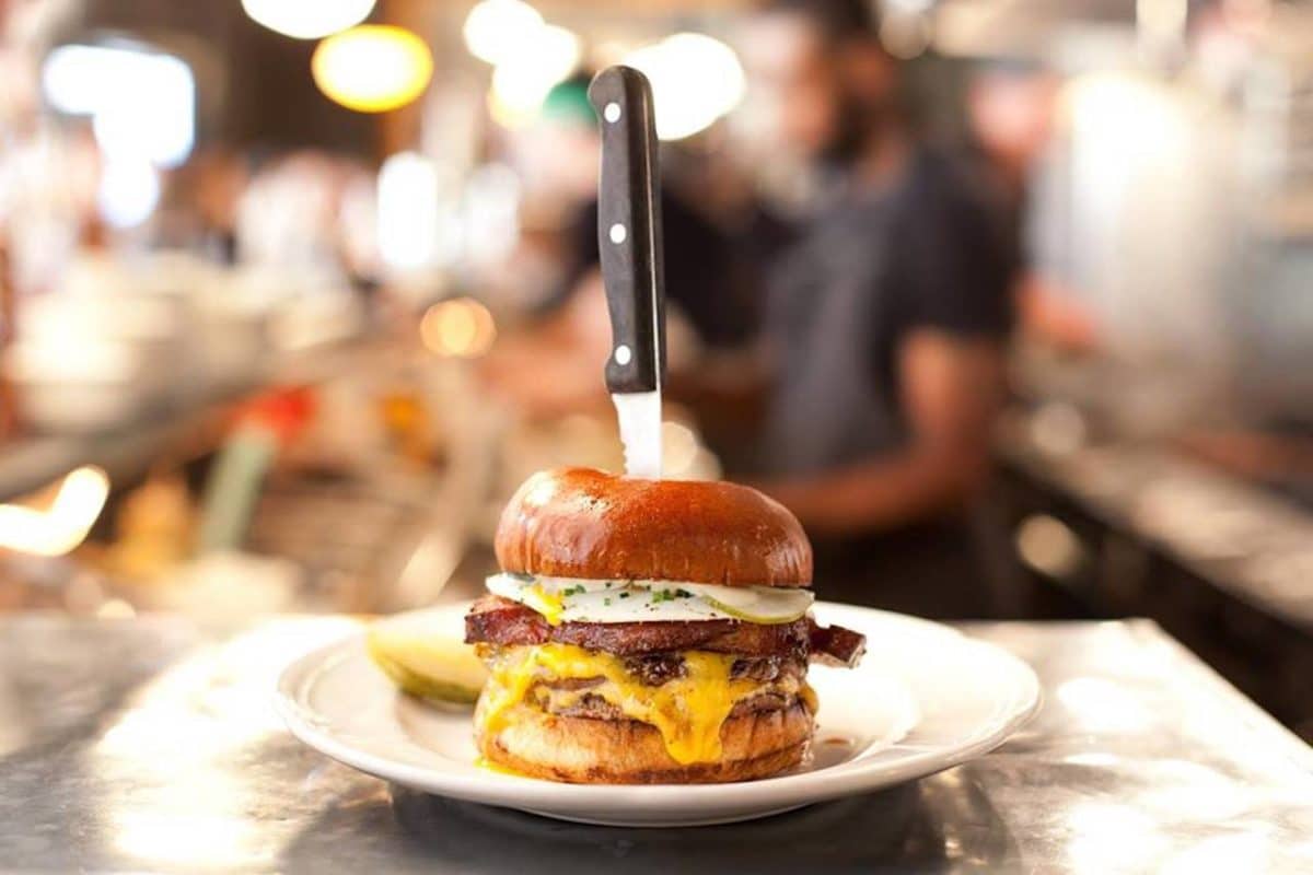 cheeseburger on white plate with steak knife in teh middle sticking straight up