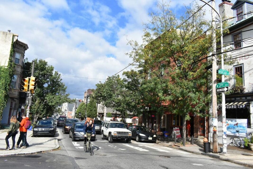 man biking on street and other people walking on sidewalk on sunny day