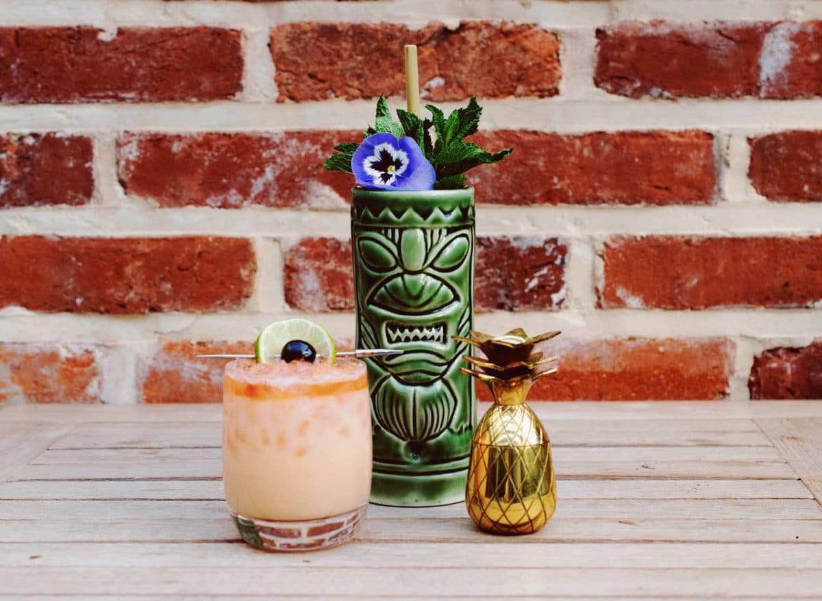three tiki cocktails sirring on table in front of brick wall