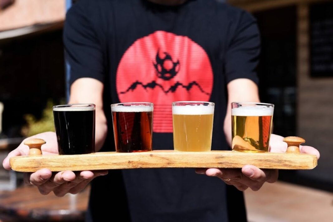 man holding four beer tasters on wooden board