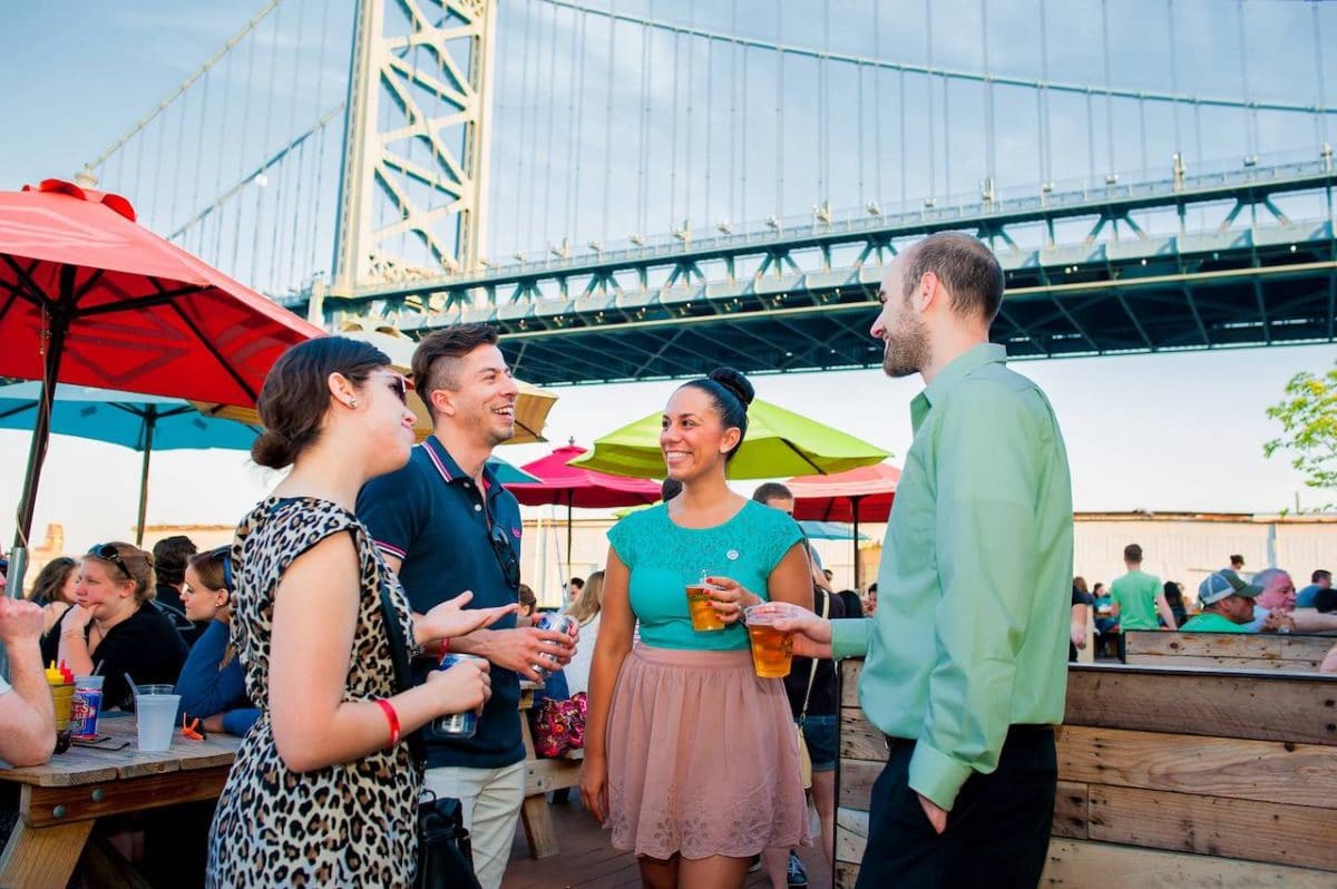 four friends drinking beers in beer garden with bridge in the background