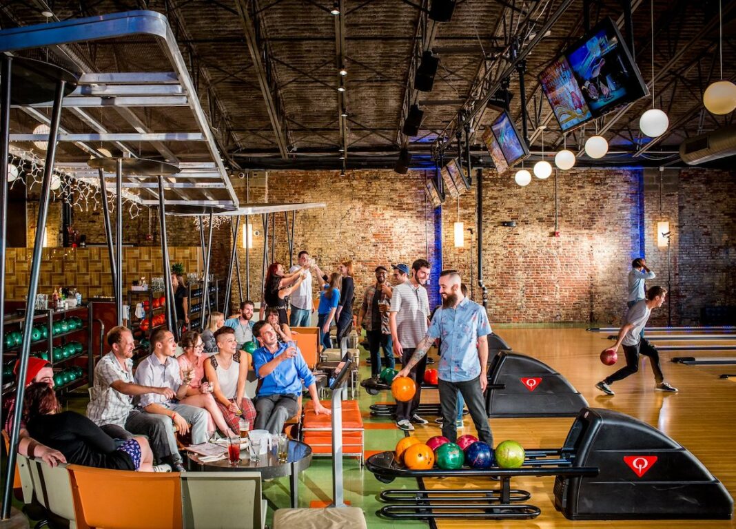 people bowling in bowling alley and drinking in booth