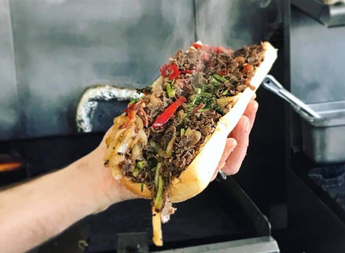 hand holding large sandiwch filled with meat and peppers