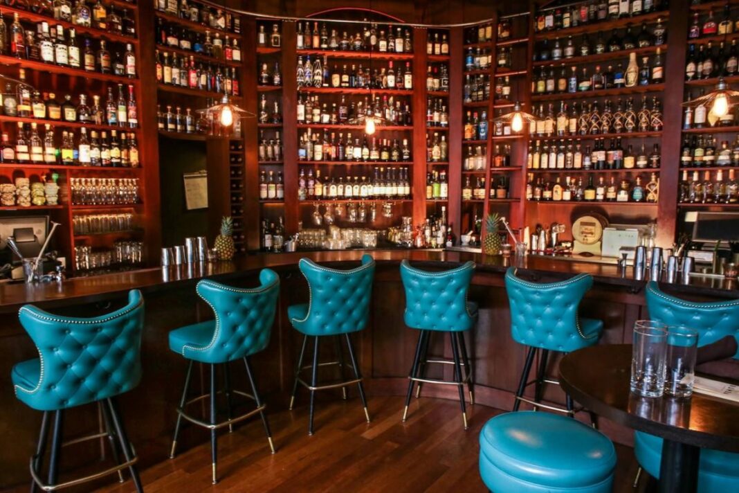 semi-circle bar with blue chairs and wall of liquor in bar behind them