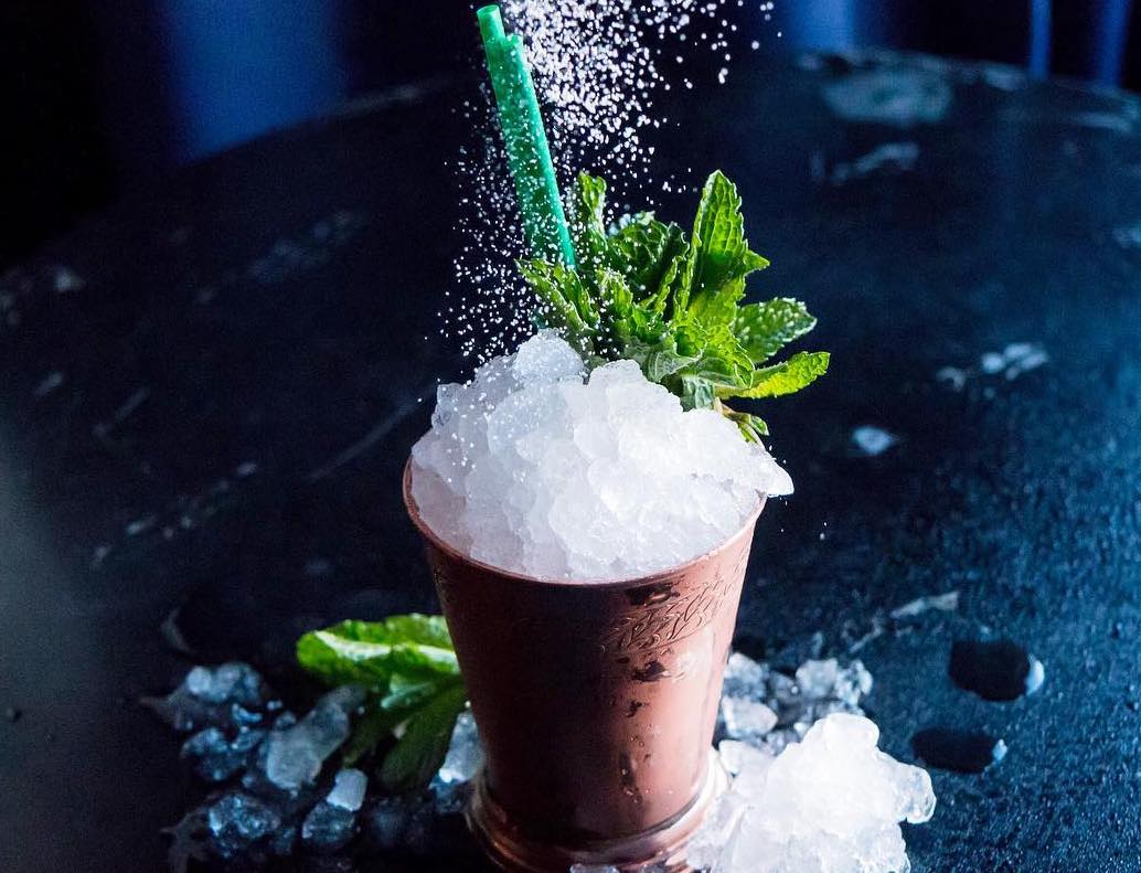 cocktail with shaved ice and green straws being sprinkled with white topping