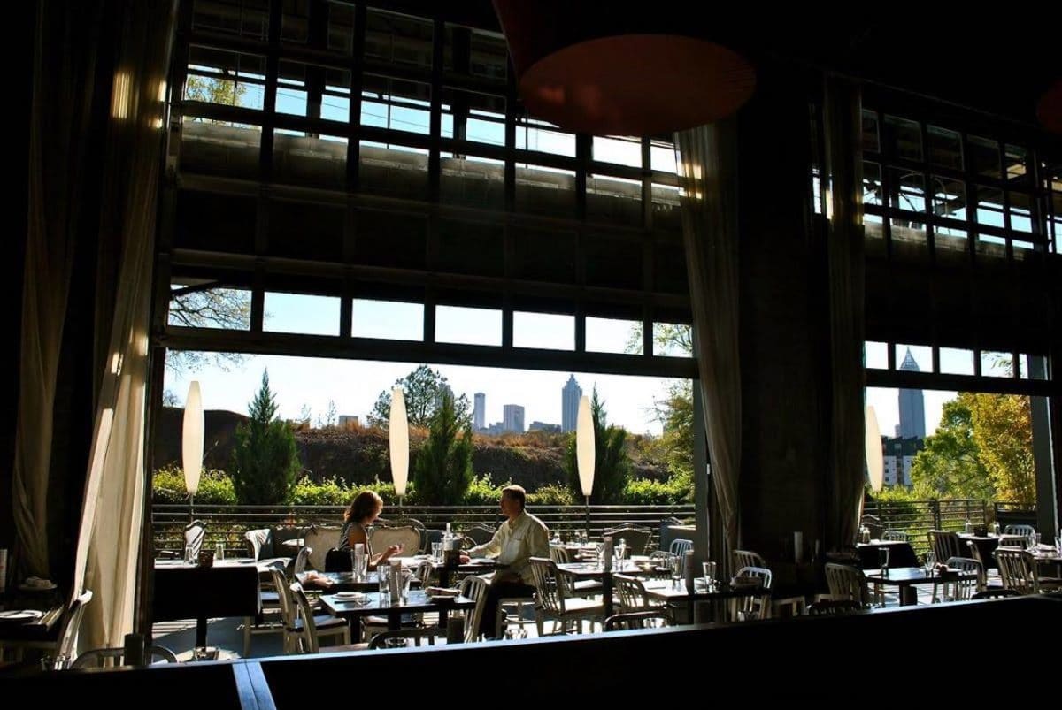 dark interior with two people sitting and drinking and eating with atlanta skyine in background