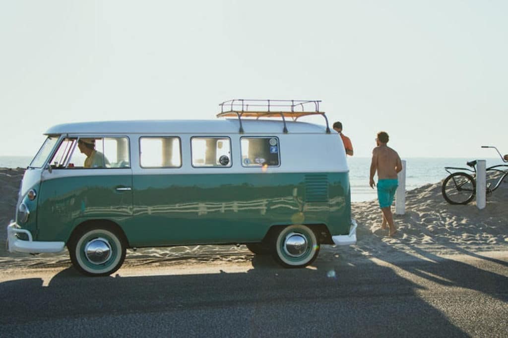 VW bus parked in front of the beach with man standing next to it