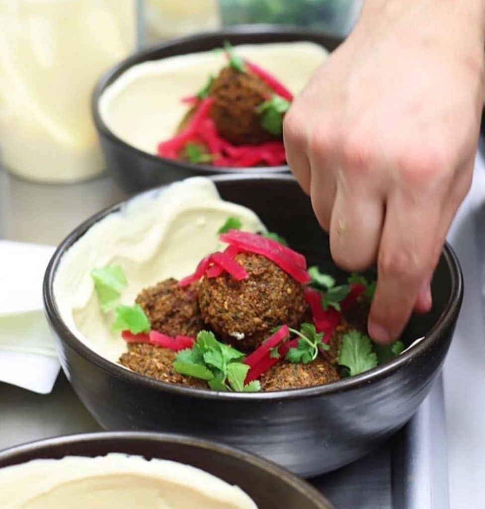 person's hand dipping into hummus and falafel bowl