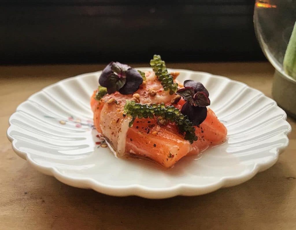 piece of raw fish on plate with other fish and toppings on it