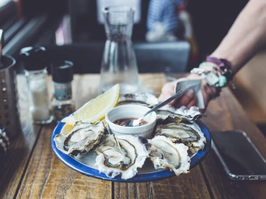person holding plate of fresh, raw oysters in shell