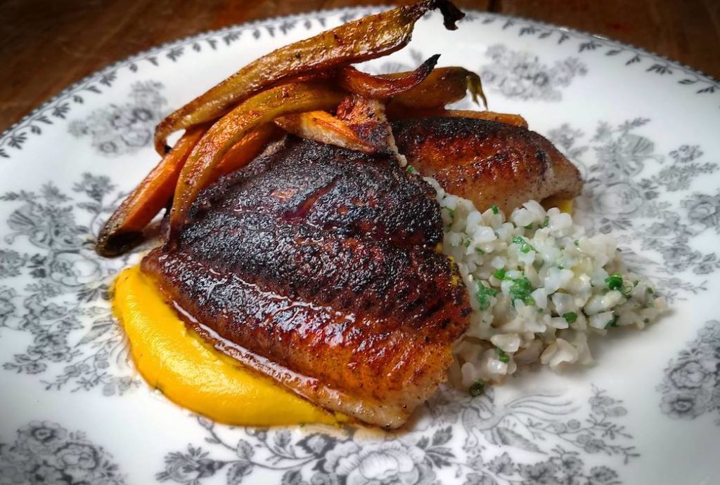 cooked fish on plate over rice and a side of yellow paste and carrots
