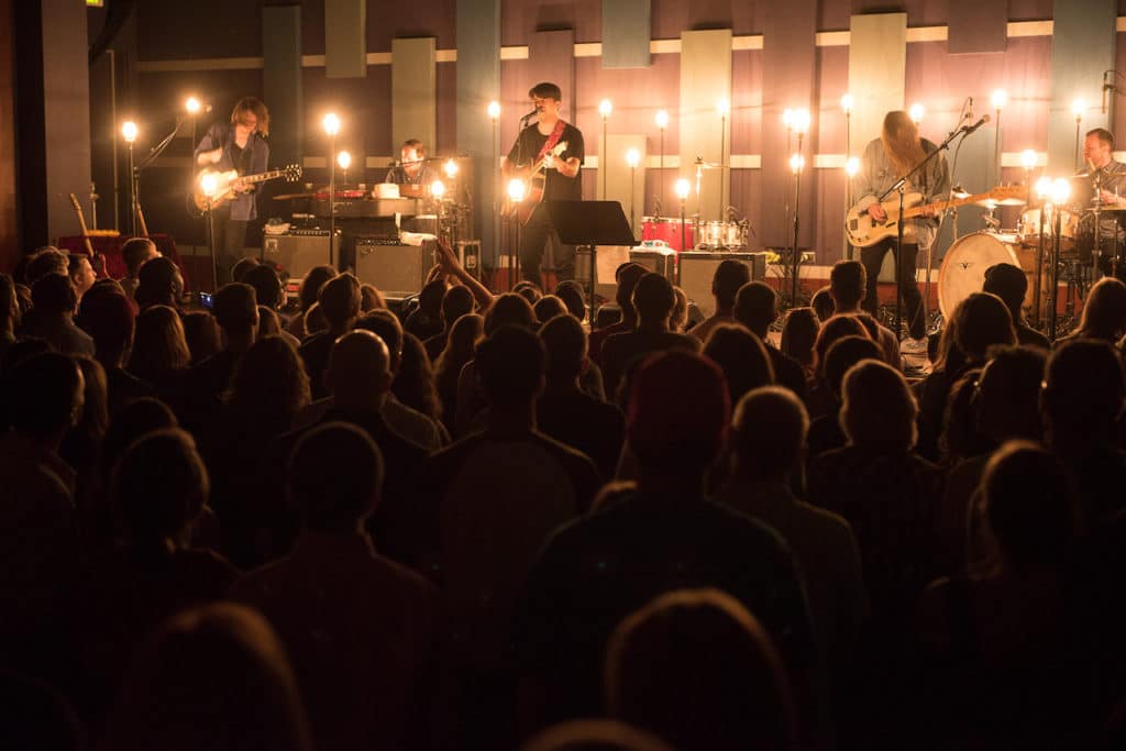 man signing on stage with lights shining on him and people in audience watching closely